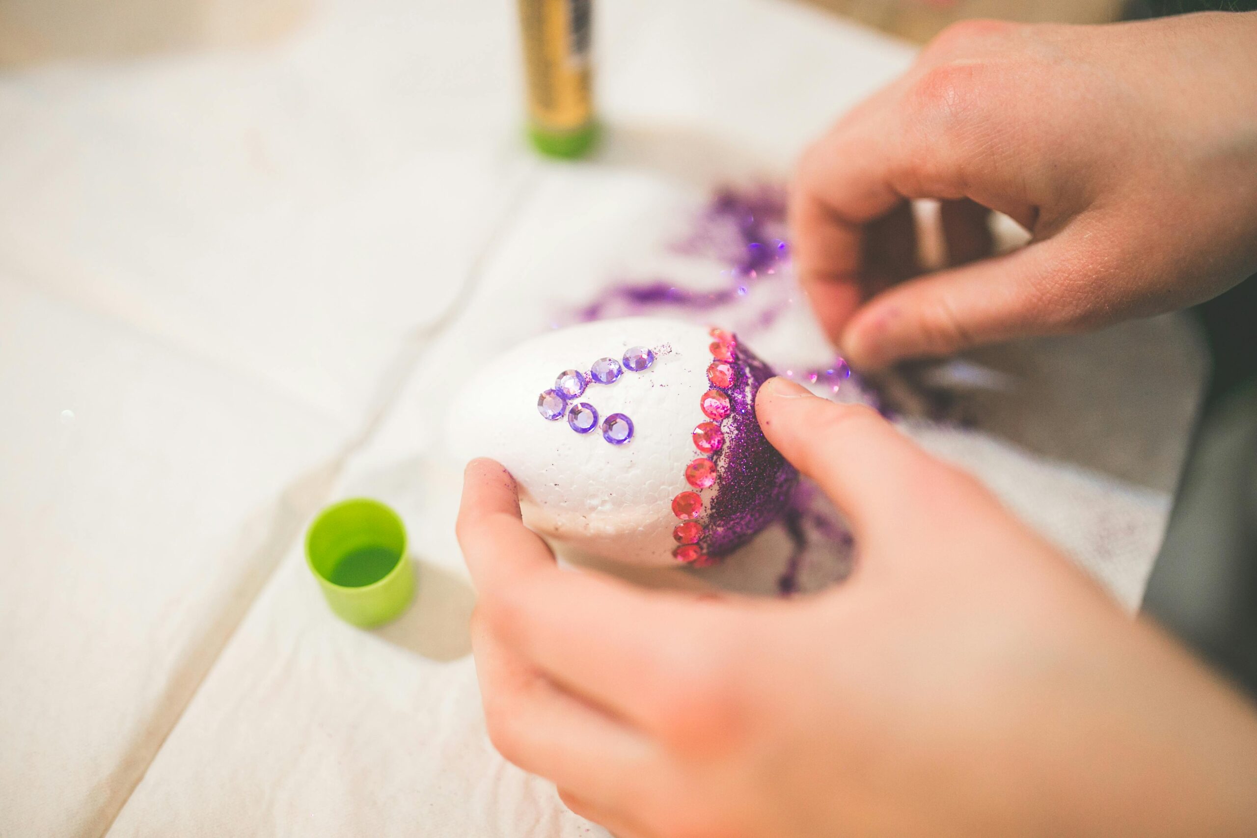 Close-up of hands decorating an Easter egg with glitter and jewels, showcasing festive creativity.